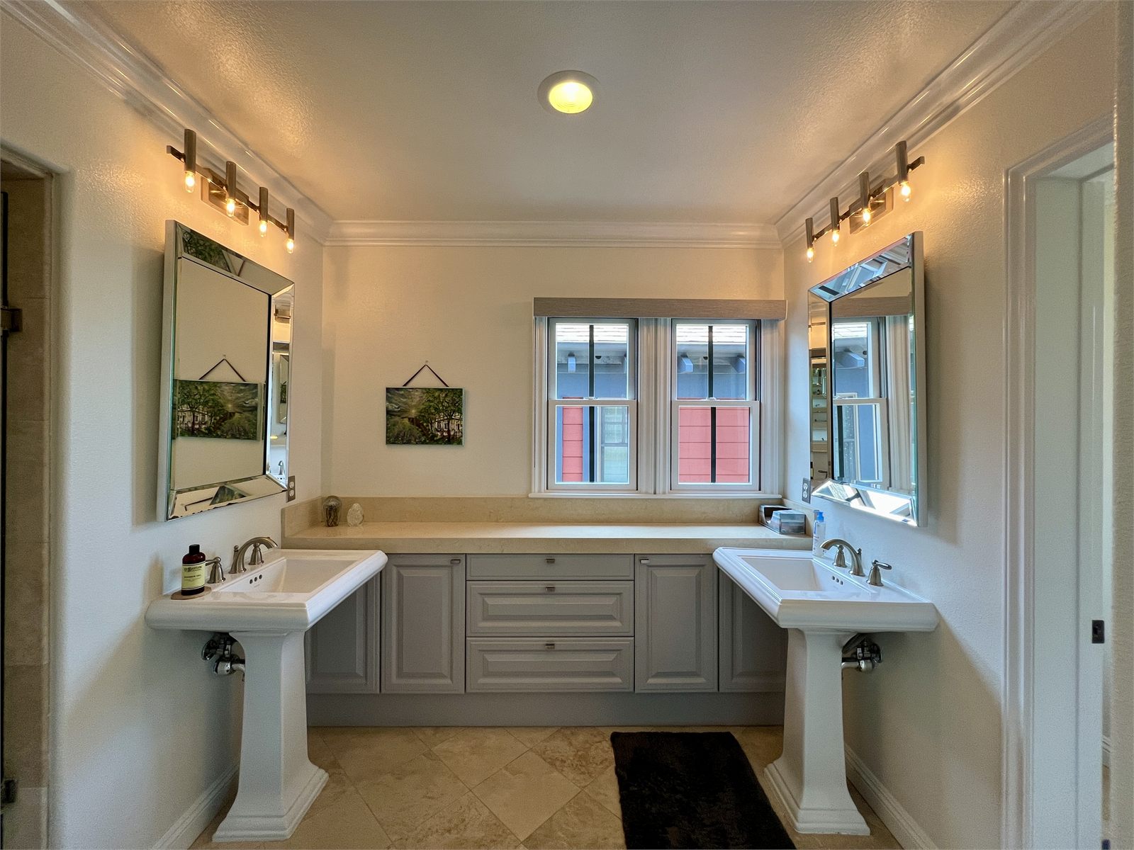 Bathroom with two separate white pedestal vanities, each under its own framed mirror and vanity light