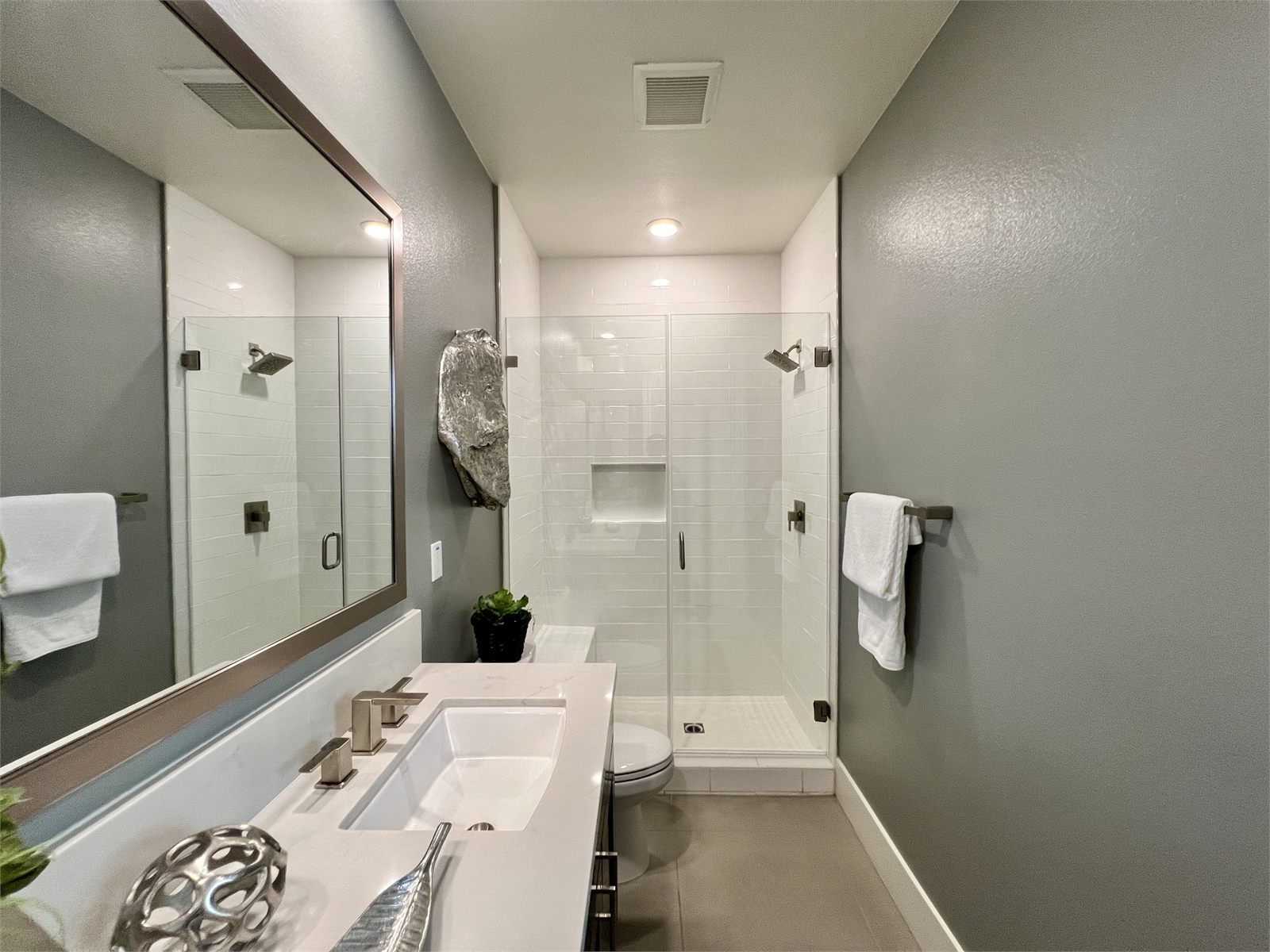 Full bath with a single white vanity, a large framed mirror, and a walk-in glass shower in white tile